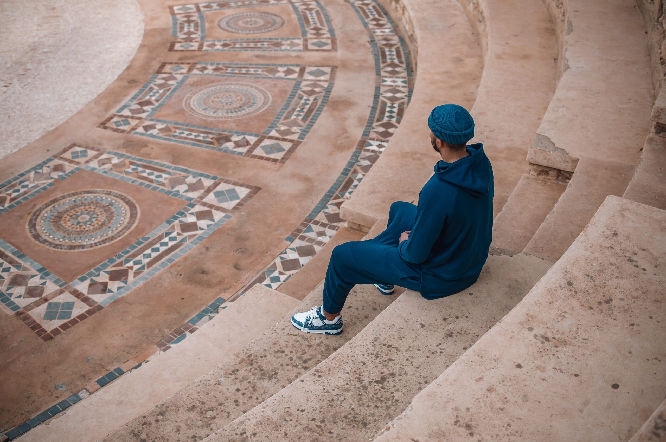 Homme en ensemble bleu assis sur les marches d’une cour au sol de zellige